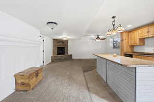 Kitchen featuring a fireplace, light carpet, light wood finish cabinetry, a ceiling fan, and open floor plan