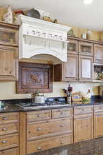 Kitchen with dark stone countertops, glass insert cabinets, stainless steel gas cooktop, and wood finish cabinetry