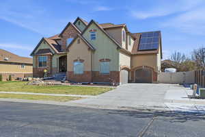 View of front of property with a gate, roof mounted solar panels, driveway, a garage, and stucco siding