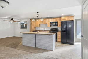 Kitchen featuring black appliances, light wood finish cabinetry, light tile patterned floors, ceiling fan, and light stone counters