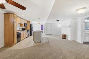 Kitchen featuring light colored carpet, black appliances, open floor plan, and hanging light fixtures
