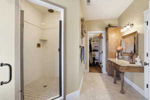 Full bathroom featuring a spacious closet, vanity, a marble finish shower, and light tile patterned flooring
