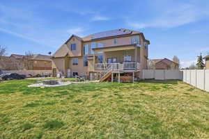 Back of house with an outdoor fire pit, solar panels, a wooden deck, a fenced backyard, and stucco siding