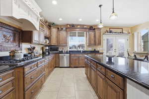 Kitchen with dark stone counters, stainless steel appliances, hanging light fixtures, wood finish cabinets, and french doors