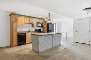 Kitchen with light tile patterned floors, light carpet, black appliances, and light wood finish cabinets