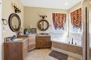 Bathroom featuring two vanities, a garden tub, light tile patterned flooring, and recessed lighting