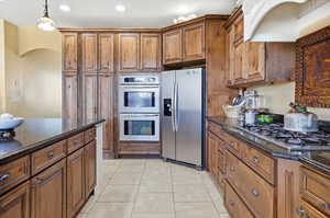 Kitchen with dark stone countertops, wood finish cabinetry, and stainless steel appliances