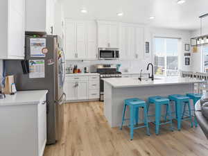 Kitchen with a kitchen breakfast bar, stainless steel appliances, white cabinets, an island with sink, and light wood-style floors