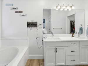 Bathroom featuring double vanity, light wood-style flooring, and a garden tub