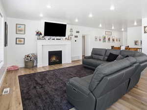 Living area with light wood-type flooring, a glass covered fireplace, and recessed lighting