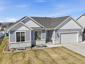 View of front of house with a front yard, a garage, driveway, and a shingled roof