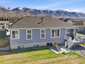 Rear view of property featuring a patio area, roof with shingles, a mountain view, a yard, and stucco siding