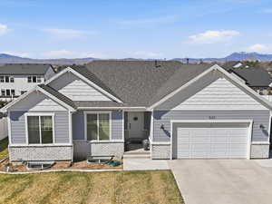 View of front of house with an attached garage, concrete driveway, a front lawn, and roof with shingles