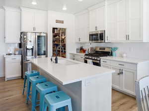 Kitchen with decorative backsplash, stainless steel appliances, an island with sink, white cabinetry, and recessed lighting