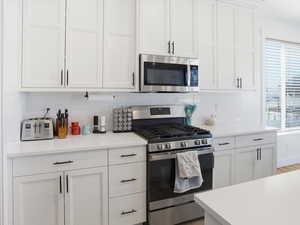 Kitchen with stainless steel appliances, white cabinetry, and tasteful backsplash