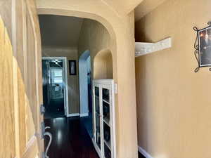 Corridor with a textured wall, dark wood-type flooring, and arched walkways