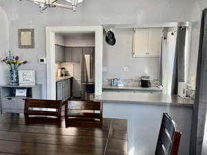 Kitchen with a textured wall, freestanding refrigerator, a peninsula, decorative backsplash, and gray cabinetry