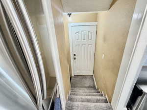 Stairway with a textured wall, a textured ceiling, and carpet