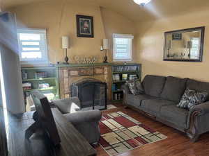 Living area with a textured wall, a fireplace, wood finished floors, and vaulted ceiling