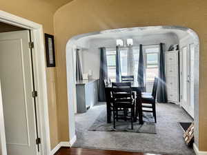 Carpeted dining space with arched walkways, a textured wall, and hanging lights
