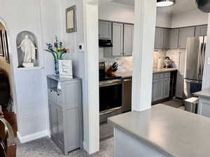 Kitchen featuring a textured wall, gray cabinets, light countertops, stainless steel appliances, and arched walkways