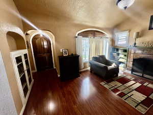 Living area featuring a textured wall, a fireplace, dark wood finished floors, built in features, and arched walkways