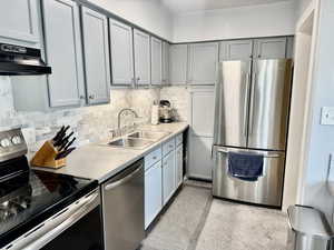 Kitchen with stainless steel appliances, light countertops, extractor fan, tasteful backsplash, and gray cabinets
