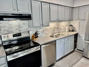 Kitchen featuring stainless steel appliances, light countertops, decorative backsplash, and gray cabinetry