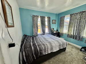 Bedroom with a textured ceiling, dark carpet, and a textured wall