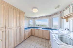 Laundry area featuring wallpapered walls, washing machine and clothes dryer, cabinet space, light tile patterned flooring, and a textured ceiling