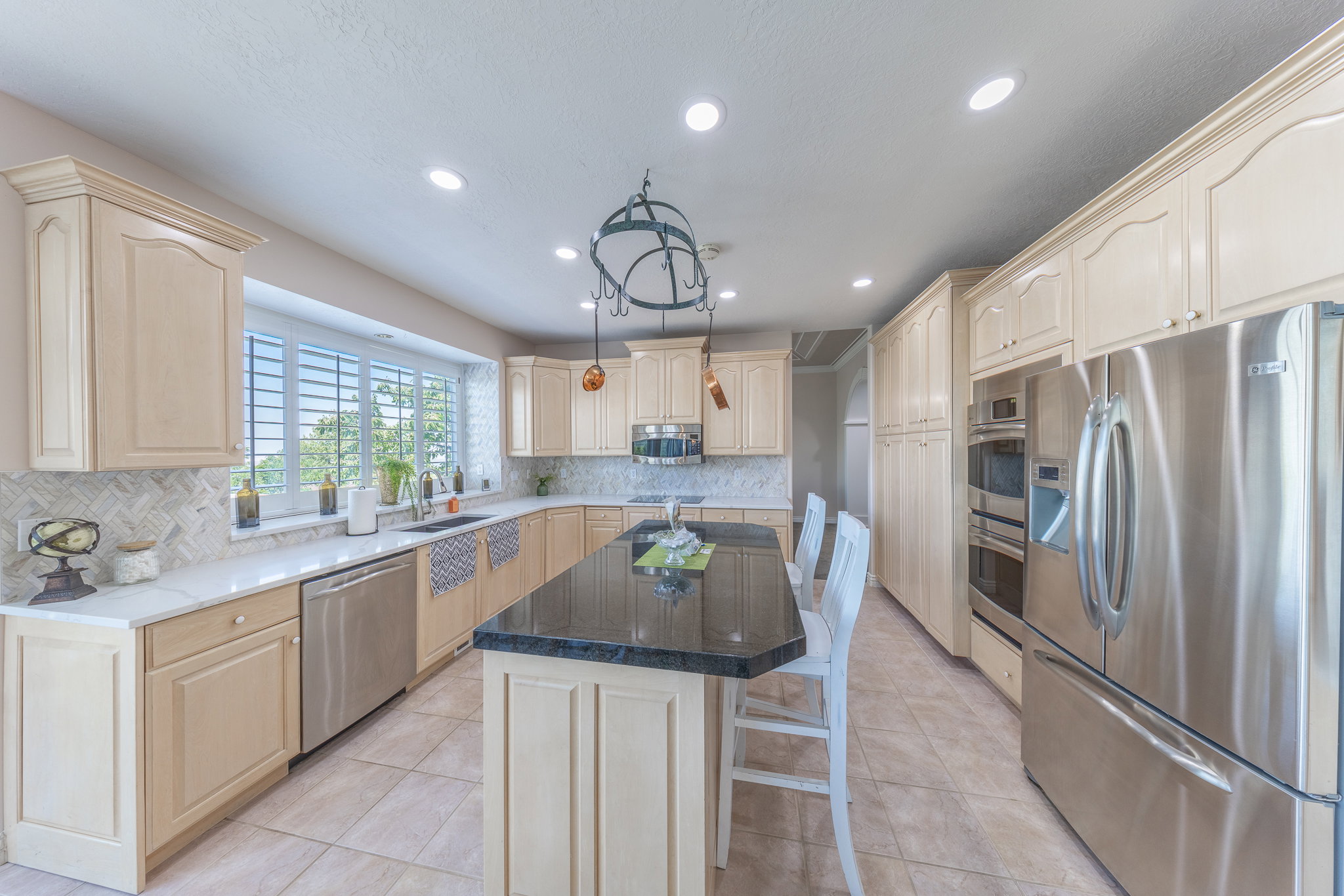 Kitchen with stainless steel appliances, light wood finish cabinets, light tile patterned floors, a center island, and recessed lighting