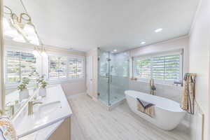 Full bathroom with double vanity, a soaking tub, a shower stall, ornamental molding, and recessed lighting