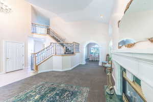 Entryway featuring dark carpet, arched walkways, a high ceiling, a glass covered fireplace, and recessed lighting