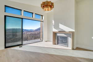 Unfurnished living room with a mountain view, a high ceiling, light wood-style flooring, a glass covered fireplace, and suspended lighting