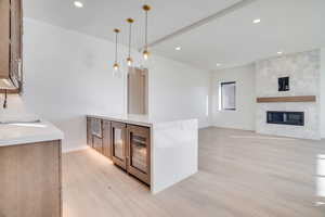 Kitchen featuring light stone counters, a peninsula, light wood-style floors, open floor plan, and wine cooler