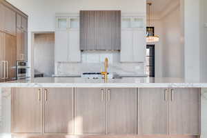 Two tone kitchen featuring two tone cabinetry, light stone countertops, decorative backsplash, and glass insert cabinets