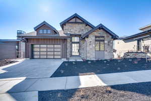 View of front of home featuring stone siding, concrete driveway, an attached garage, and roof with shingles