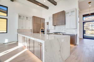 Kitchen featuring two tone color scheme, light stone counters, a large island, tasteful backsplash, and glass insert cabinets
