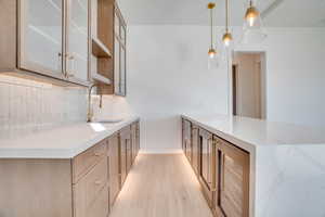 Kitchen featuring a peninsula, light stone countertops, light wood finished floors, and pendant lighting