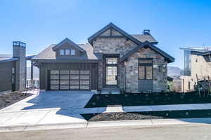 View of front of property with stone siding, driveway, an attached garage, and roof with shingles