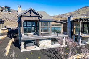 Back of house featuring a chimney, a patio area, a mountain view, and stone siding