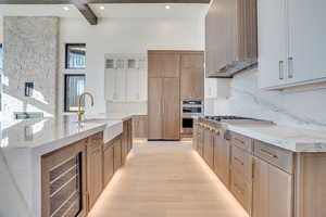 Dual tone kitchen with dual tone cabinetry, light stone counters, beverage cooler, backsplash, and a large island with sink