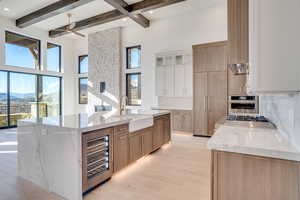 Kitchen with light stone countertops, two tone color scheme, backsplash, a large island with sink, and wine cooler