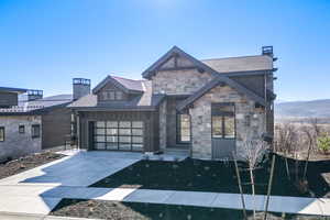 View of front of home featuring concrete driveway, a chimney, stone siding, and an attached garage