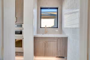 Kitchen with tile walls, double oven, and light stone counters