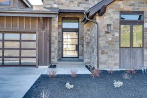 Property entrance with stone siding, board and batten siding, concrete driveway, and a garage