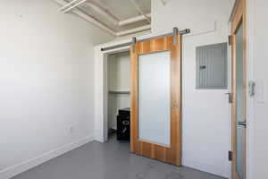 Unfurnished bedroom featuring a barn door, finished concrete flooring, electric panel, and a closet