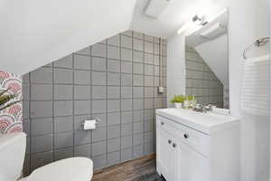 Bathroom with tile walls, vanity, lofted ceiling, and dark wood-type flooring