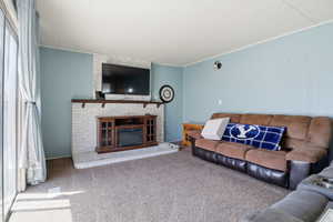 Carpeted living room featuring a brick fireplace and crown molding