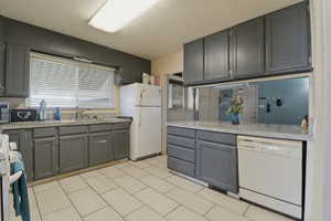 Kitchen with white appliances, gray cabinetry, light stone countertops, and a peninsula